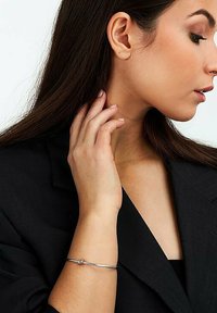 Bracciale a manica in argento indossato su un polso, caratterizzato da un design attorcigliato con un piccolo dettaglio a nodo. Lo sfondo è neutro e poco invadente.