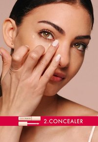 Tubo de corrector con aplicador junto a una persona aplicando el producto debajo del ojo. Tonos de piel naturales, textura suave, fondo neutro.