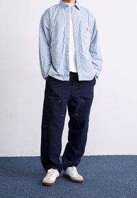 Světle modrá proužkovaná košile na knoflíky s náprsní kapsou, ve spojení s tmavě modrými nákladními kalhotami s kapsami a bílými botami. Texturovaná tkanina.