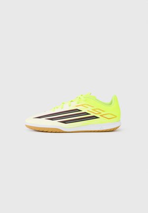 Indoor soccer shoe in neon yellow with black stripes, gum rubber sole, and "F50" text on the side against a plain white background.