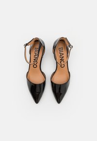 Zapatos de tacón alto de charol negro con punta afilada, correas en el tobillo y plantillas beige con el nombre de la marca "BIANCO".