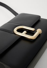 Borsa nera in pelle con chiusura a patta, caratterizzata da un evidente fermaglio a forma di C dorato, texture liscia e dettagli di cucitura minimi.