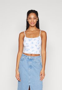 Top corto blanco con un patrón floral en azul claro, con tirantes finos y tela recogida. Combinado con una falda de mezclilla de tiro alto.
