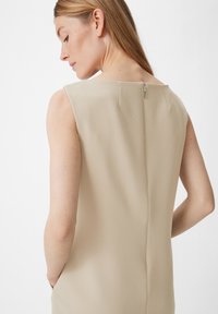 Beiges ärmelloses Kleid aus strukturiertem Stoff, mit rundem Ausschnitt und einem Reißverschluss im Rücken. Es hat eine klare Silhouette und seitliche Taschen.