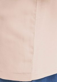 Top beige a maniche corte con una texture liscia, caratterizzato da un orlo dritto e dettagli di cucitura discreti, abbinato a jeans denim blu.