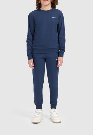Donkerblauwe katoenen sweatshirt en bijpassende broek, geribbelde boorden, logo in het wit, met een ronde halslijn en slim fit, gedragen met witte sneakers.