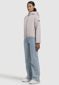 Light gray puffer jacket with a hood, featuring a front zipper, side pockets, and elastic cuffs, paired with light blue straight-leg jeans and white shoes.