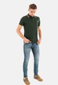 Groene polo met gele accenten, gemaakt van een katoenmix, gecombineerd met blauwe slim-fit jeans en bruine sneakers. Ontworpen met een logo op de borst.