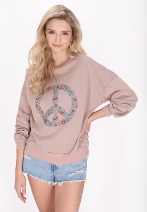 Felpa a maniche lunghe di colore rosa chiaro con un design di simbolo di pace floreale. Presenta una vestibilità ampia e polsini a coste, abbinata a pantaloni corti in denim strappati.