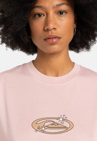 Lyserød T-shirt lavet af blødt stof, med et grafikdesign i guld og sort af en bølge og stjerner på fronten. Rund halsåbning.