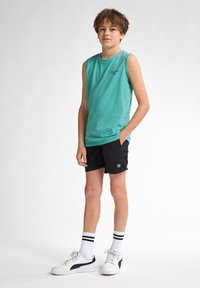 Turkisærmeløs skjorte, sorte shorts med logo, hvide sneakers med sorte accenter, og hvide sokker med sorte striber.