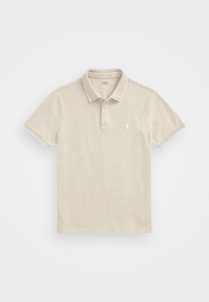 Beige polo skjorte med tynne hvite detaljer, korte ermer og krage. Har en liten, brodert logo på venstre bryst. Teksturert stoff.