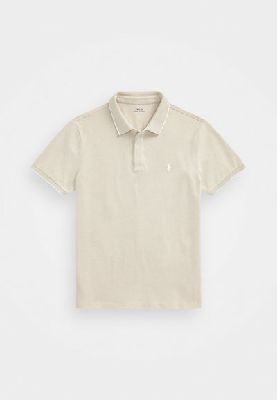 Camisa polo bege com finas apostas brancas, mangas curtas e colarinho. Apresenta um pequeno logo bordado no lado esquerdo do peito. Tecido texturizado.