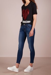 Camiseta negra con un diseño de corazón de lentejuelas rojas y texto blanco, combinada con jeans skinny azules y zapatillas blancas.