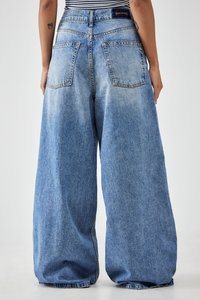 Wijdvallende blauwe denim jeans met een vervaagde textuur, twee achterzakken en een logo patch op de tailleband.