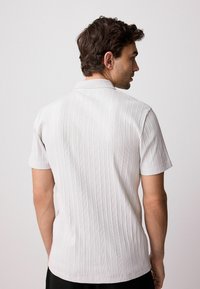 Short-sleeve, collared shirt in light gray with vertical stripes, featuring a textured fabric and a relaxed fit. Displayed from the back.