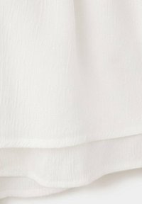 Tissu blanc texturé, superposé de plis doux et d'un ourlet légèrement incurvé sur un fond clair.