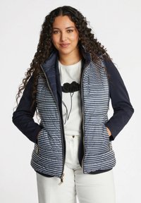 Marineblauer und gestreifter Steppweste mit Reißverschluss, Seitentaschen und taillierter Passform; kombiniert mit einem weißen Shirt mit floralem Grafikdesign.