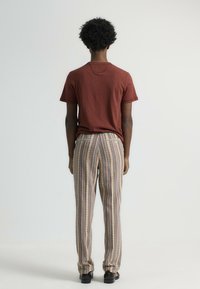 Camiseta roja de manga corta combinada con pantalones holgados a rayas que presentan un patrón texturizado y un detalle de bolsillo trasero. Unos zapatos negros completan el conjunto.