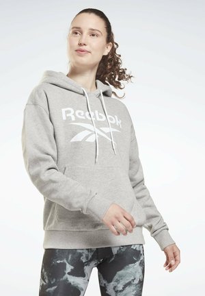 Grijze hoodie met een wit Reebok-logo, voorzien van een trekkoordcapuchon en een voorkantzak. Draagt met zwart en grijs gestreepte leggings.