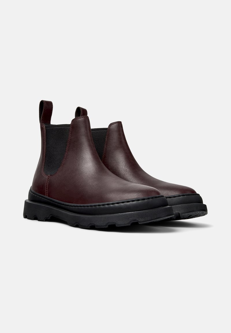Brown leather Chelsea boots with elastic sides, black textured rubber sole, and pull tabs for easy wear. Smooth finish with stitched detailing.