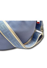 Ronde, lichtblauwe leren tas met een gestructureerde afwerking. Voorzien van een patroonriem in blauw en beige met gouden accenten.