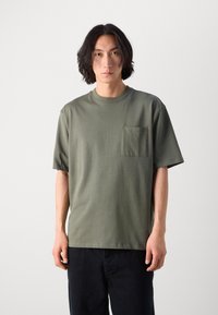 T-shirt à manches courtes vert olive avec un col rond et une poche poitrine, confectionné en tissu doux, présentant une coupe décontractée et un design simple.