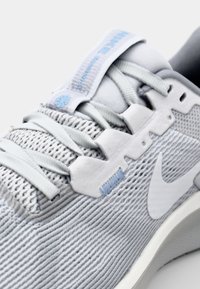 Helle graue Sneaker mit strukturiertem Mesh-Obermaterial, verstärkten Ösen und einem weißen Swoosh-Logo. Mit weichen Schnürsenkeln und einem schlanken Profil.