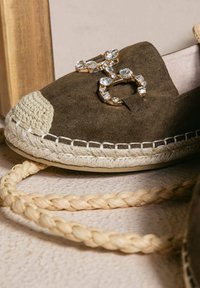 Espadrillas in suede marrone con suola in juta intrecciata. Presentano un accento gioiello in tonalità dorate. Bordo intrecciato in beige chiaro sulla punta.