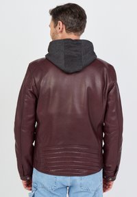 Burgunderfarbene Lederjacke mit grauer Kapuze, die eine glatte Textur, gerippte Akzente auf dem Rücken und Druckknopfverschlüsse an den Manschetten aufweist.