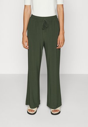 Woman wearing dark green wide-leg pants with elastic waistband and drawstring, paired with white open-toe sandals and a white top.