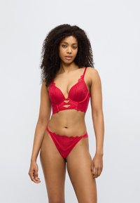 Σετ εσώρουχα σε κόκκινο χρώμα με δαντελωτό σουτιέν με βαθύ ντεκολτέ και κοψίματα, συνδυασμένο με αντίστοιχο δαντελωτό στρινγκ. Μαλακή υφή.