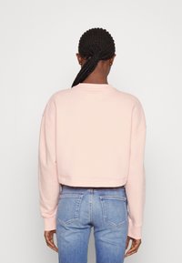 Sudadera corta rosa con mangas largas, textura suave y cuello redondo, combinada con jeans azul claro que muestran detalles de los bolsillos.