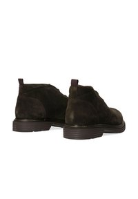 Stivaletti in suede marrone scuro con punta rotonda, caratterizzati da cuciture a contrasto e una suola in gomma testurizzata. Due linguette sul retro.