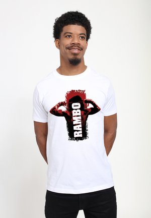 Hvid bomulds t-shirt med et grafisk design af en muskuløs figur i sort og rød med ordet "RAMBO" i fede bogstaver.