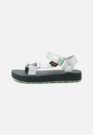 Sandalo sportivo con cinturini argentati metallici, suola nera texturizzata e accenti verde chiaro, mostrato di profilo su sfondo bianco.