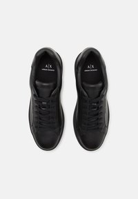 Baskets en cuir noir avec une finition lisse, bout rond, design à lacets et logo embossé sur la languette et le côté. Esthétique minimaliste.