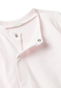 Měkký růžový dětský overal s patentkami podél předního dílu a malou vyšitou králíčkovou aplikací na hrudi poblíž výstřihu.