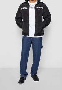 Czarna puchowa kurtka z logo "KARL" i "KANI", biała koszulka, niebieskie dżinsy oraz czarne trampki. Widoczna pikowana faktura.