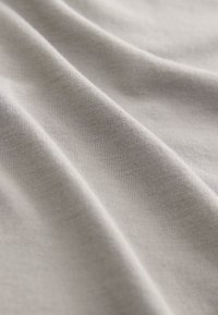 Light gray fabric with a soft texture, exhibiting smooth, flowing folds and a fine ribbed pattern.