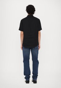 Μαύρο κοντομάνικο πουκάμισο, άνετη εφαρμογή, ορατή υφή υφάσματος. Συνδυασμένο με μπλε τζιν, ίσια γραμμή, με λεπτή φθορά, και μαύρα παπούτσια.