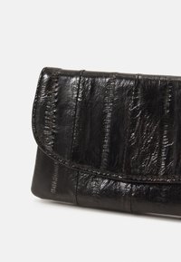 Black leather clutch with a textured, glossy finish. Features stitched detailing and a curved flap closure. Compact rectangular shape.