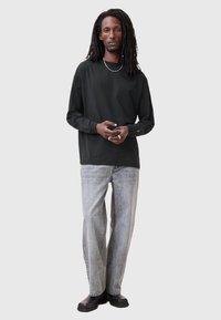 Maglietta nera a maniche lunghe con una vestibilità comoda, abbinata a jeans a gamba larga grigio chiaro e calzature nere, creando un look casual.