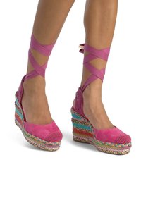 Tacchi a zeppa con tomaia in suede rosa e accenti lavorati a maglia. La suola in espadrilles intrecciata e colorata aggiunge texture e interesse visivo.