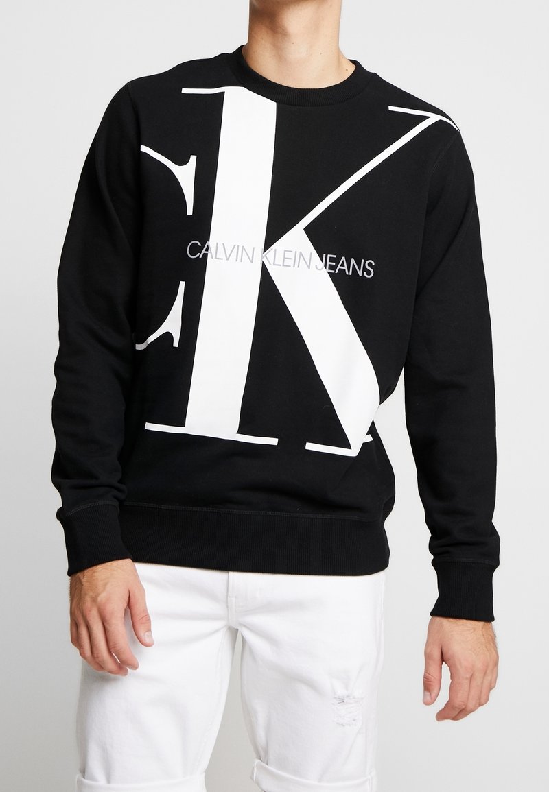 Felpa nera in cotone, con una grande grafica bianca "CK" e il testo "CALVIN KLEIN JEANS". Polsini e orlo a costine.