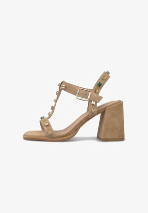 Sandalia beige de ante con punta abierta, tacón ancho, correa en el tobillo con cierre de hebilla, y adornos de gemas multicolores y tachuelas metálicas.