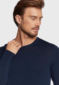 Mornarsko modra rebrasta pulover s okroglim izrezom in dolgimi rokavi. Diskreten logotip na prsih. Mehak material in prilega.