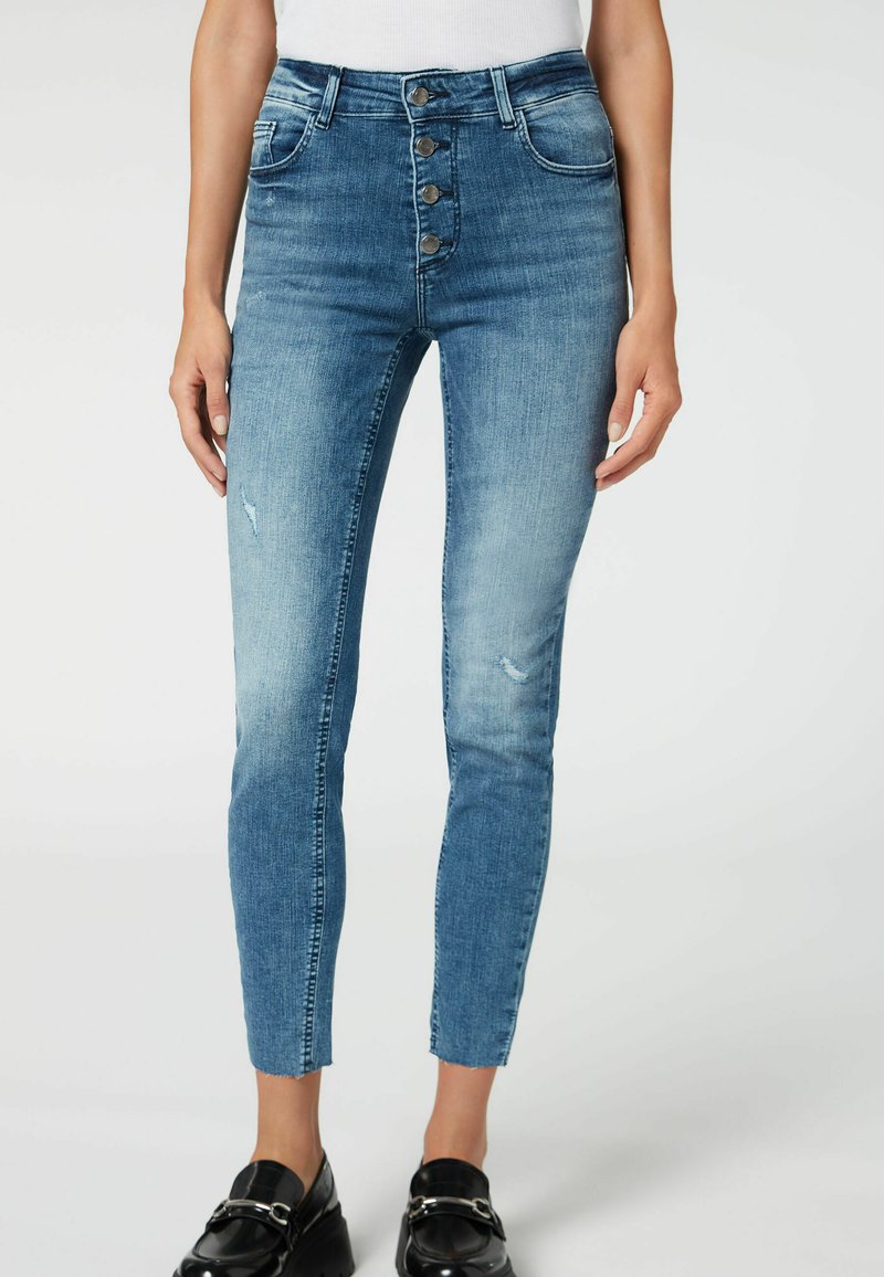 Höga blå denimjeans med en urblekt tvätt, femknappsstängning och lätt slitage nära knäna. Beskuren modell i ankellängd.