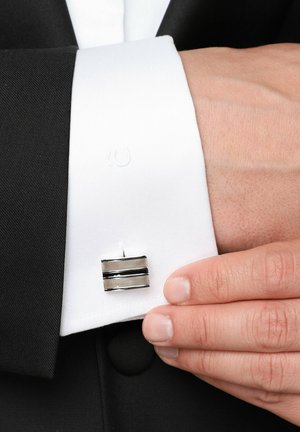 Mankiet na białej koszuli z czarnymi akcentami, o prostokątnym kształcie z teksturowanym srebrnym wzorem i czarnymi paskami.