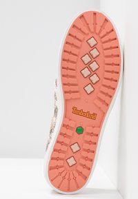 Semelle d’une basket avec un motif rose saumon, des motifs carrés et rectangulaires beige, un hexagone vert et un logo Timberland orange.